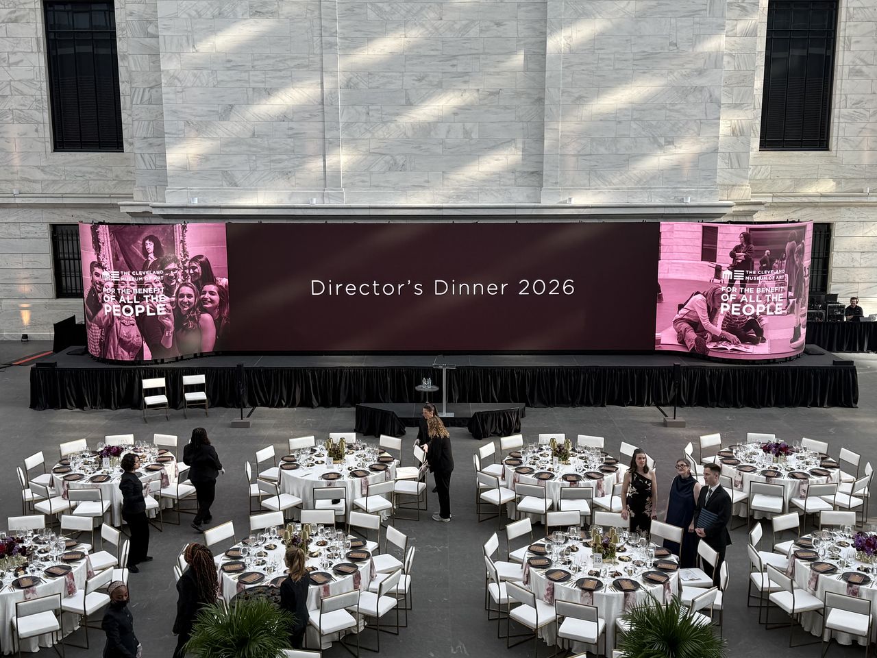 A wide curved LED wall above a black-skirted stage, overlooking a floor of set banquet tables