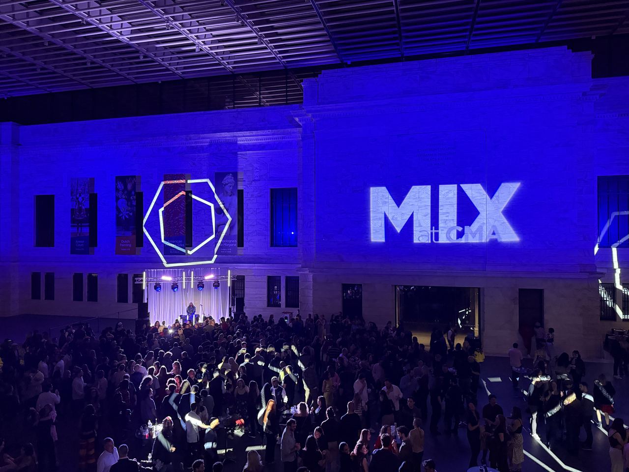 A packed museum atrium washed in blue light with projected branding and a live stage
